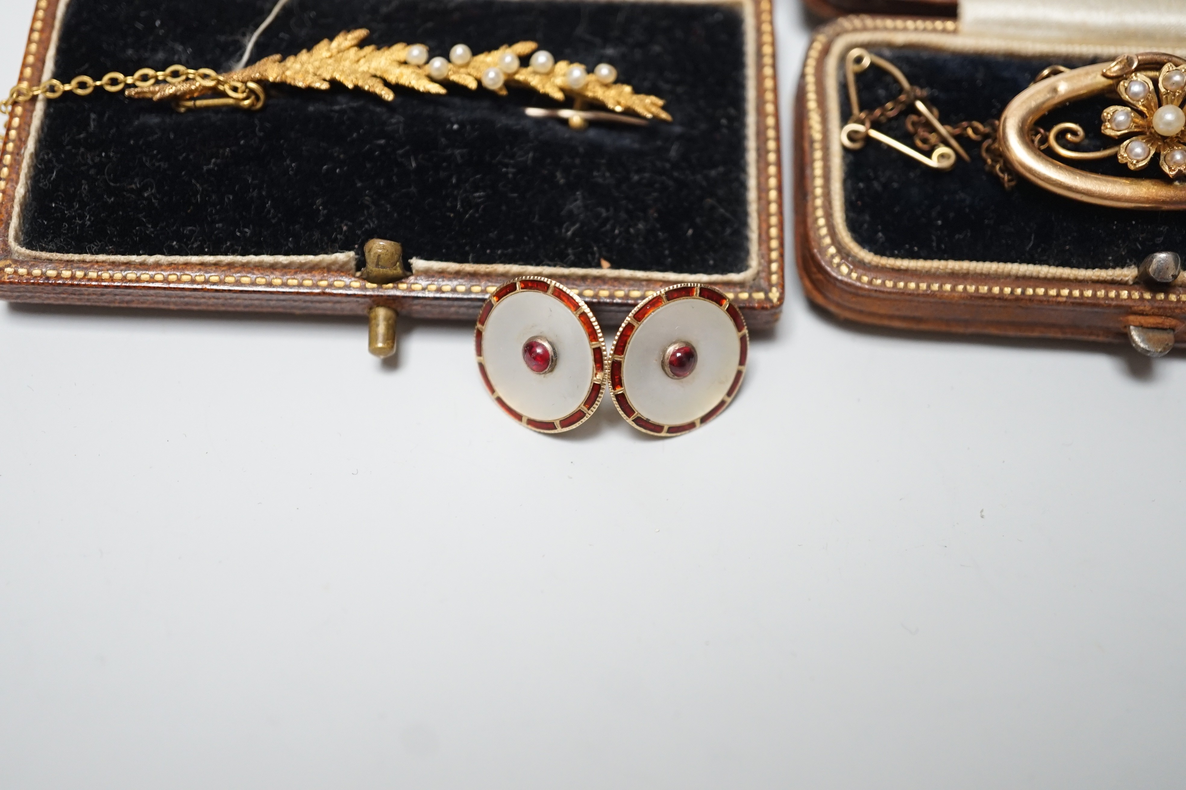 An early 20th century 15ct and seed pearl set leaf brooch, 51mm, one other 15ct and seed pearl brooch and a pair of 15ct, enamelled and gem set ear studs (converted buttons), gross weight 10 grams.